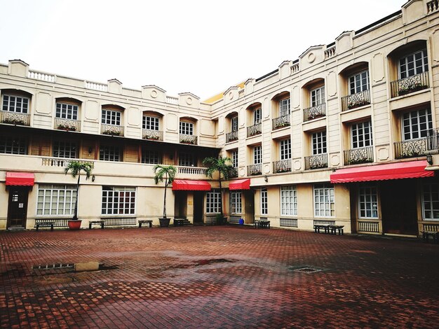 Three-story beige building with balconies, red awnings, and an open brick courtyard.