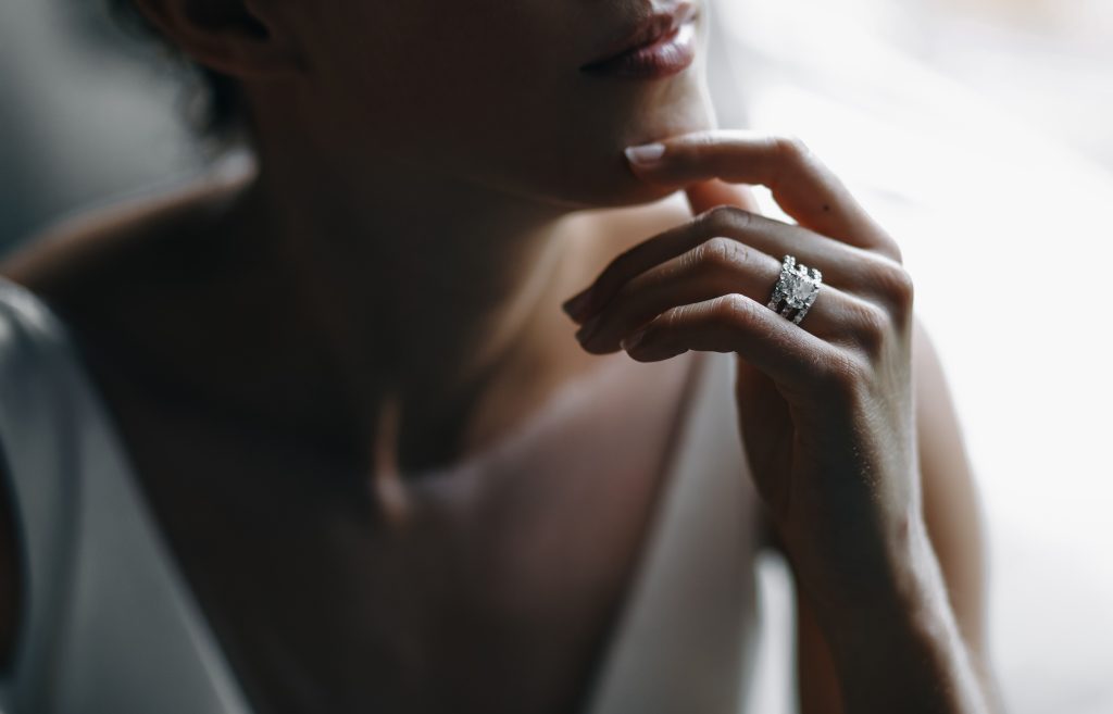 Closeup of woman wearing sparkling diamond rings on finger near her face.