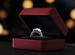 Elegant diamond ring displayed inside a red velvet jewelry box with soft lights