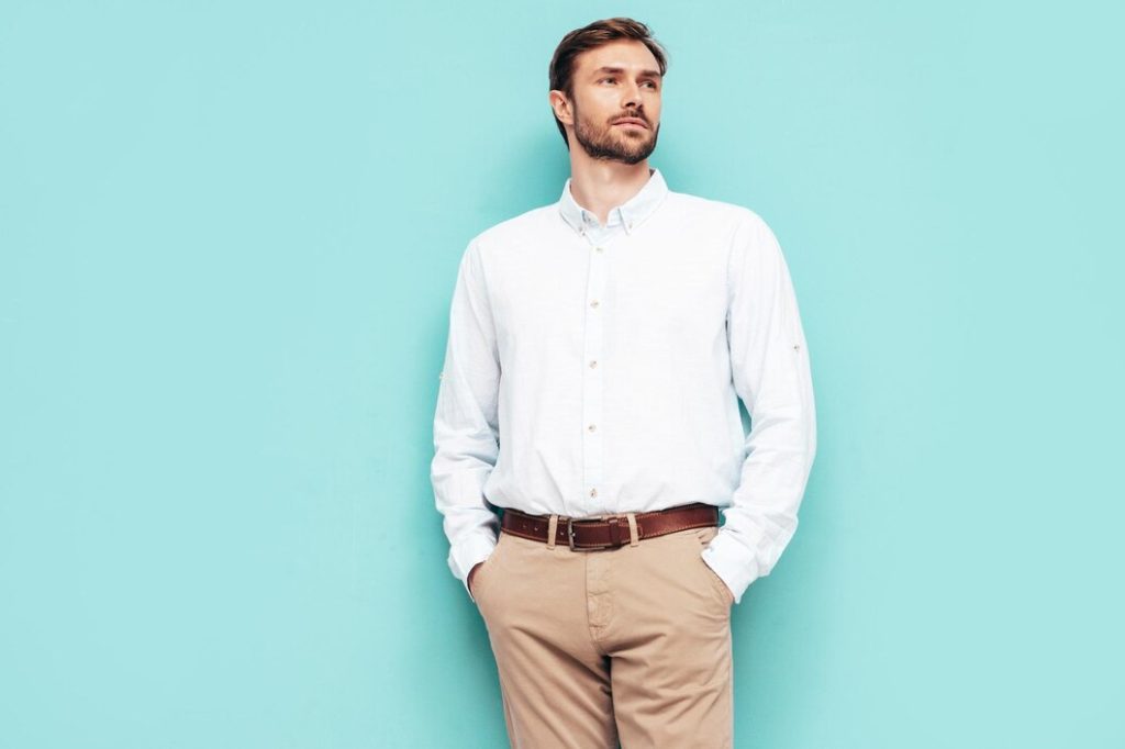 A man in a crisp white shirt and beige trousers stands confidently against a vibrant turquoise background.